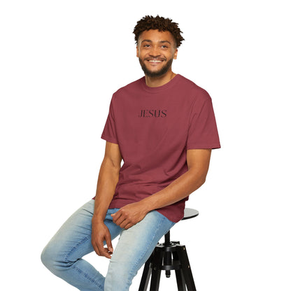 Man sitting on a stool wearing a burgandy organic cotton tshirt with the words JESUS centred.